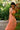 Person wearing a peach dress stands gracefully among lush greenery.