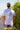 Person wearing a white t-shirt with palm tree design and text on the back, standing outdoors.
