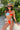 Model posing in a colorful bikini and straw hat in a tropical setting.