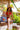 A woman in a red bikini and straw hat sitting on a wooden ledge with tropical foliage in the background.