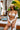 A woman in a white bikini and straw hat relaxing by a poolside cabana.