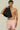 A young man with curly hair wearing a black towel and pink patterned swim shorts, standing confidently.