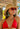 Woman in a red bikini, straw hat, and sunglasses, with statement earrings, set against a tropical backdrop.