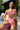 Person in a pink bikini sitting outside holding a colorful clutch.