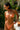 Woman in an orange bikini adjusting her swimwear in a lush outdoor setting.