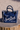 Frayed denim tote bag with 'Saint Barth' text on sandy background