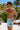 Man wearing light blue swim shorts with a graphic design, standing outdoors with palm trees in the background.