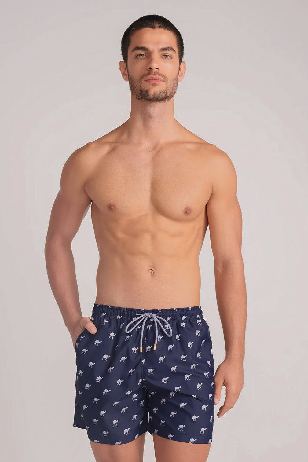 Man wearing navy blue swim shorts with patterns, standing against a plain background.