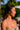 Profile of a woman with long hair wearing jewelry, set against a tropical background.