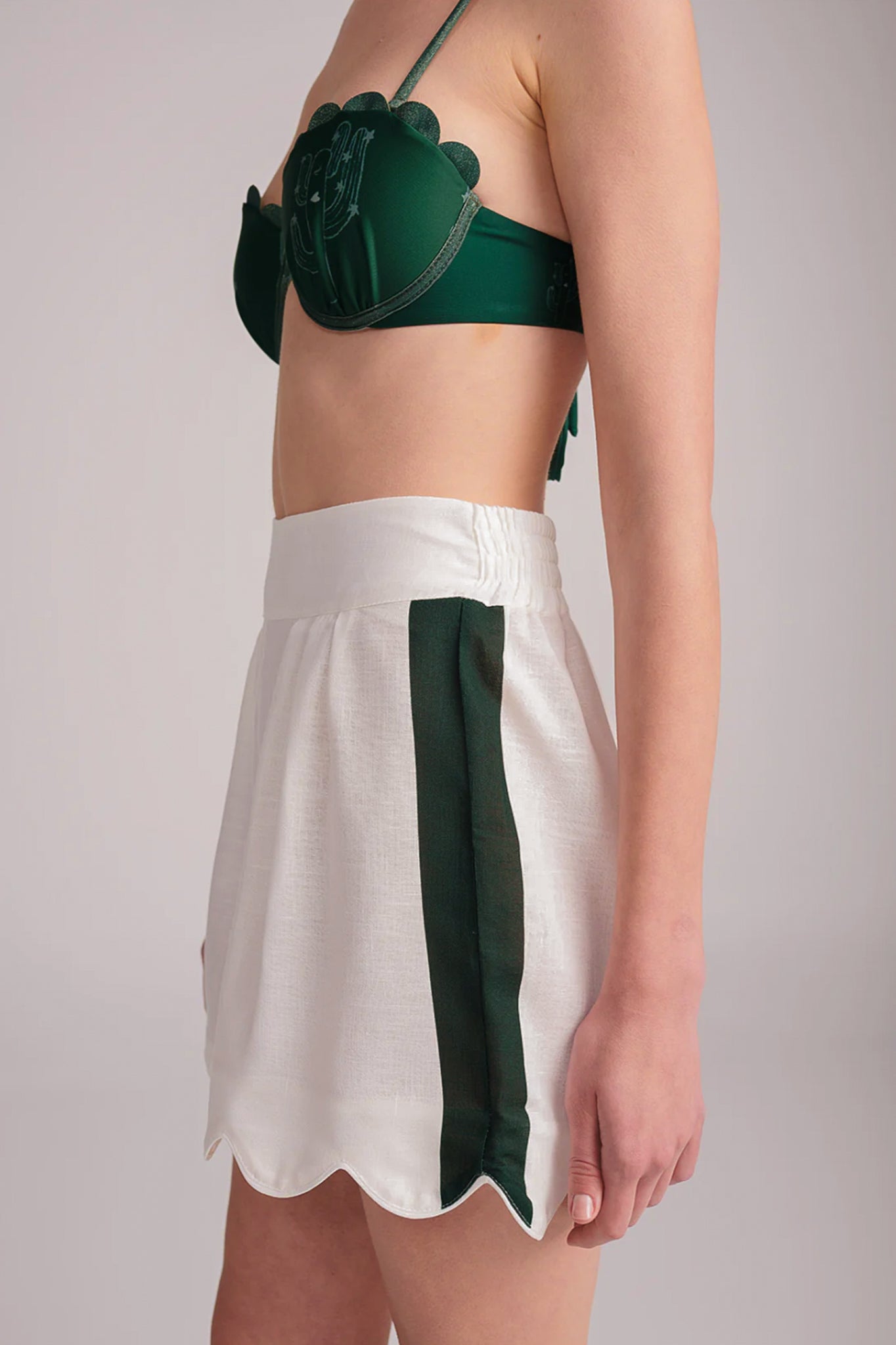 Model wearing a green bikini top and white scalloped skirt with a green stripe