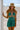A woman in a teal swimsuit and hat stands on the beach, smiling.