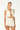 A woman modeling a white two-piece summer set consisting of a sleeveless cropped vest with tassel trim and matching drawstring shorts, against a plain white studio background.