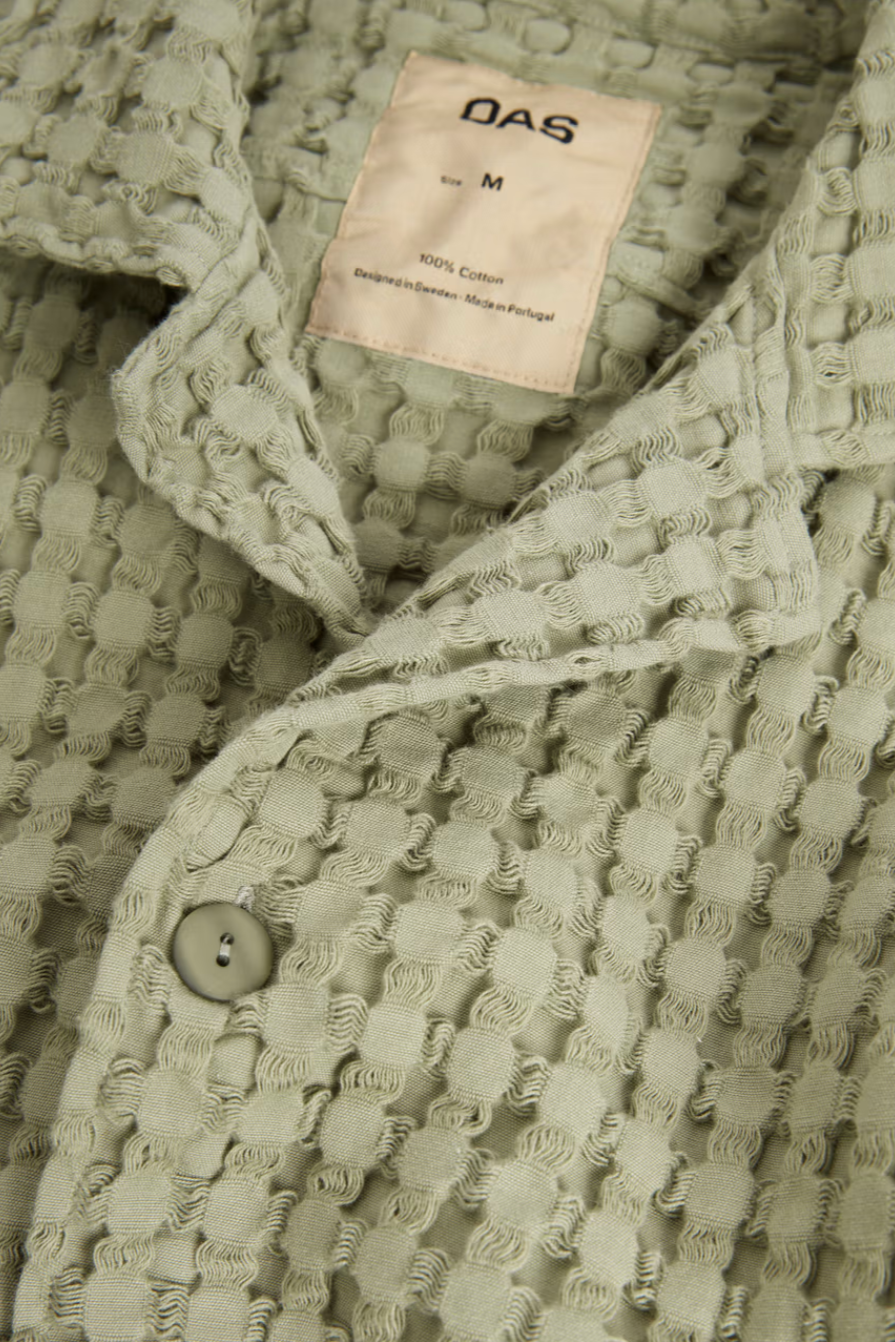 Close-up of a textured green garment with a brand label on a matching background