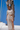 A woman stands on a white boat deck under a clear blue sky, wearing a light beige textured knit two-piece outfit with a short-sleeve crop top and a wrap-style high-slit maxi skirt.