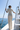 A woman stands on the deck of a sailboat wearing a cream-colored textured knit two-piece set, viewed from behind as she looks out toward the open sea under a clear blue sky.
